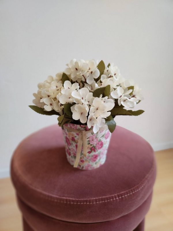 Cubo Lily sobre una butaca violeta, un cubo forrado en tela de flores con hortensias artificiales en tono crema.
